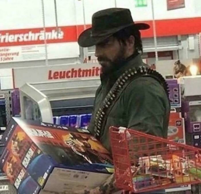 Man dressed like a cowboy holding a boxed video game inside a store, chuckling as part of funny pictures that go hard.