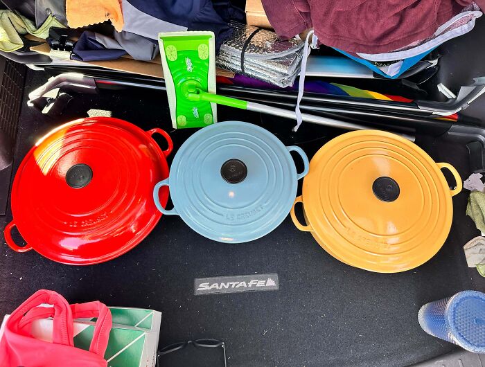 Red, blue, and yellow cast iron pots inside a car trunk showcasing thrift store jackpot finds by lucky shoppers.