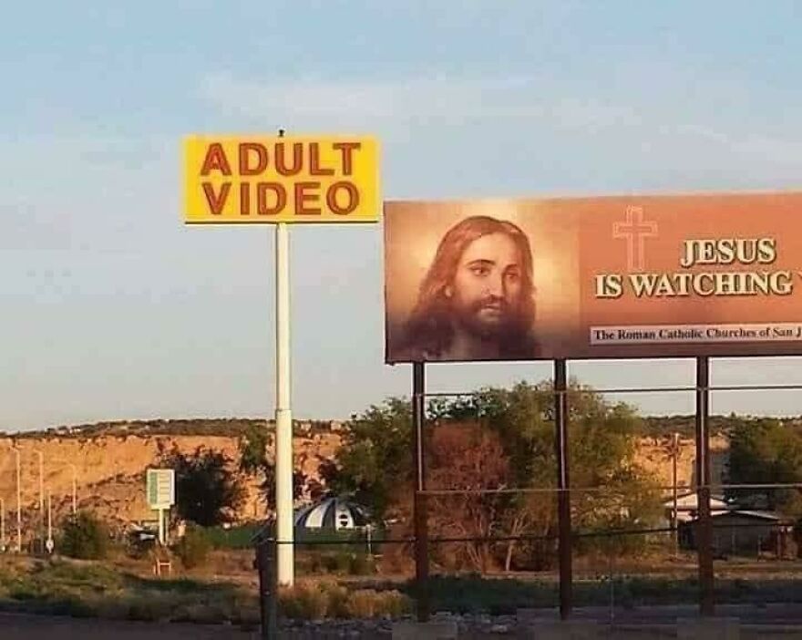 Signs for adult video store next to a religious billboard saying Jesus is watching, showcasing times people knew what they were doing.
