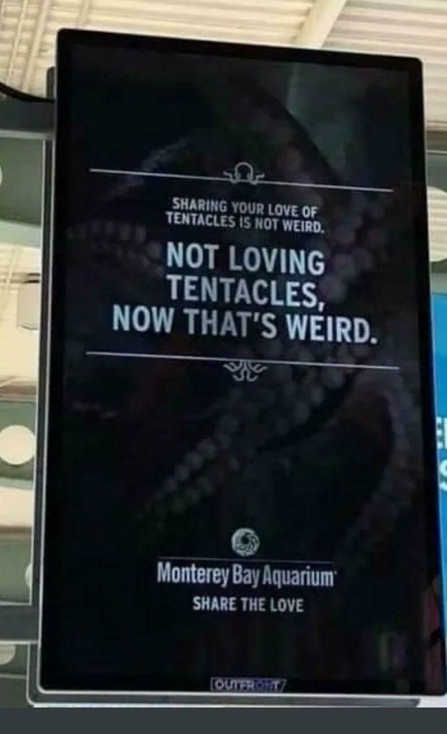 Sign at Monterey Bay Aquarium humorously promoting love for tentacles, showing people knowing what they were doing and still going for it.