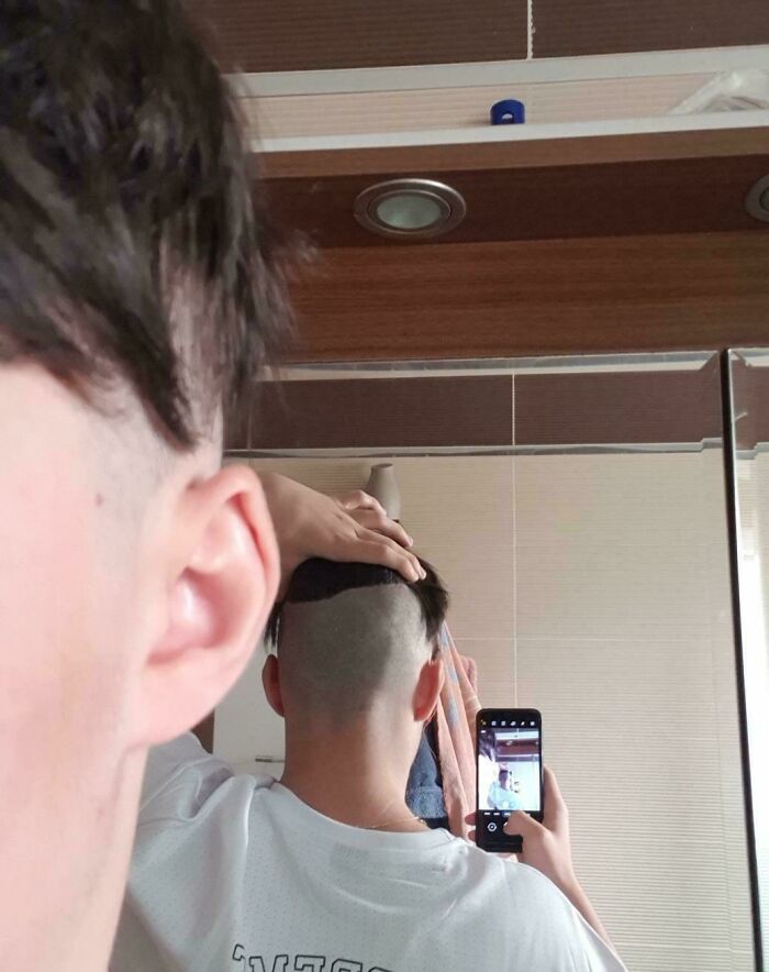 Person taking a mirror selfie showing a hilariously tragic hair accident with half their head shaved unevenly.