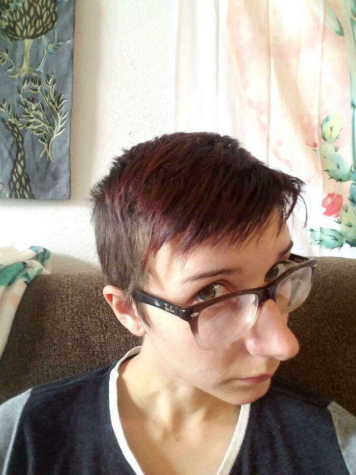 Person with short hair showing a hilariously tragic hair accident wearing glasses and sitting on a couch indoors.