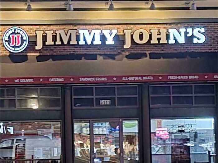 LED sign for Jimmy John's sandwich shop brightly lit on a brick storefront at night
