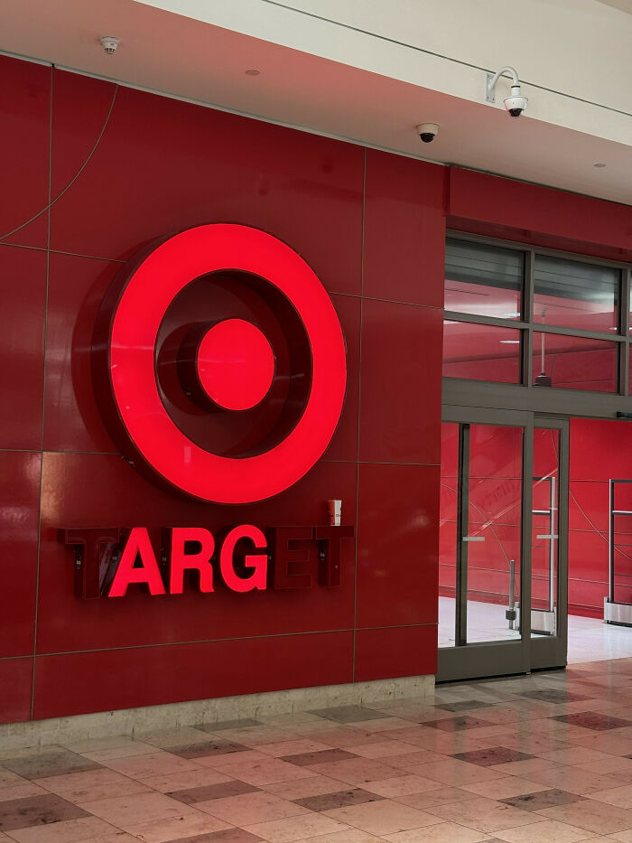 LED sign of Target store logo in red on a mall wall near glass entrance with reflective tiled floor in front.