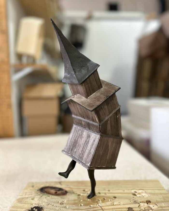 Surreal collage of a walking building sculpture with wooden textures and a pointed roof balancing on one leg.