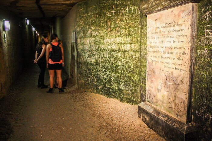 Two people exploring a dimly lit underground tunnel covered in graffiti at a spooky destination for Halloween visitors. Two people exploring a dimly lit underground tunnel covered in graffiti at a spooky destination for Halloween visitors.