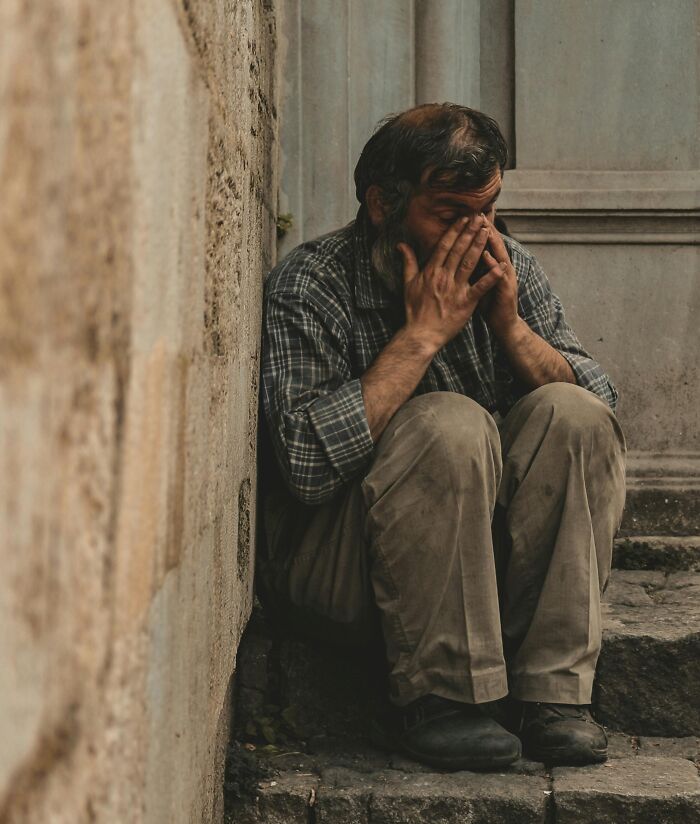 Man sitting on street steps with head in hands, evoking emotions related to unusual college courses and life challenges.
