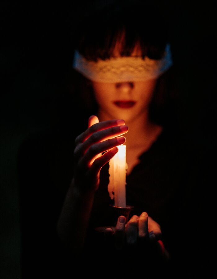 Person blindfolded holding a lit candle in darkness, creating a mysterious atmosphere for college courses concept.