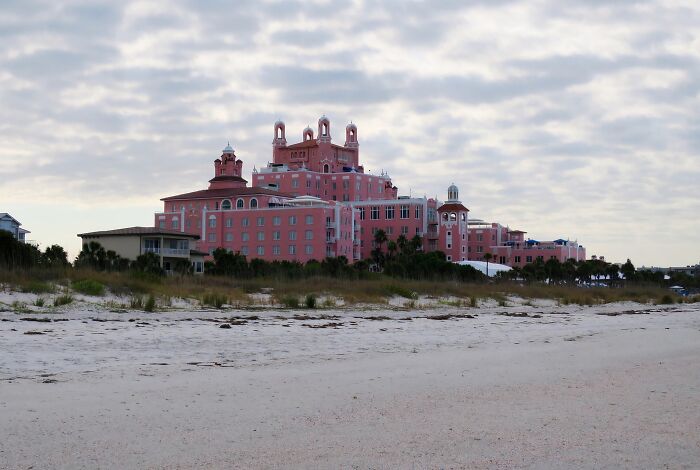 Historic pink hotel on a beach with cloudy sky, one of the spooky destinations haunting visitors this Halloween season