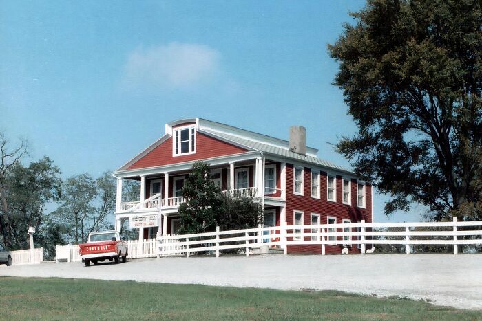 Historic red haunted house with white fence and vintage truck, a spooky destination perfect for Halloween visits.