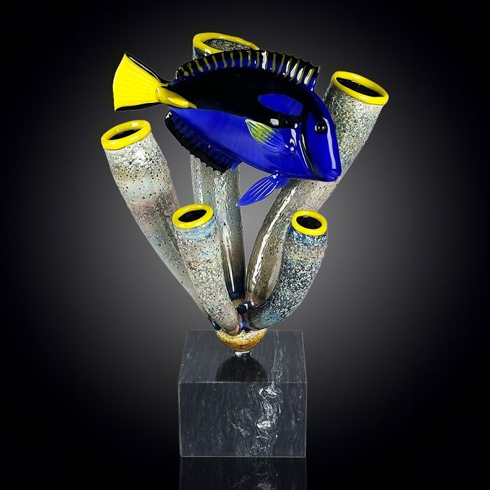 Glass sculpture of a vibrant blue and yellow fish among coral branches, showcasing stunning ocean life artistry.