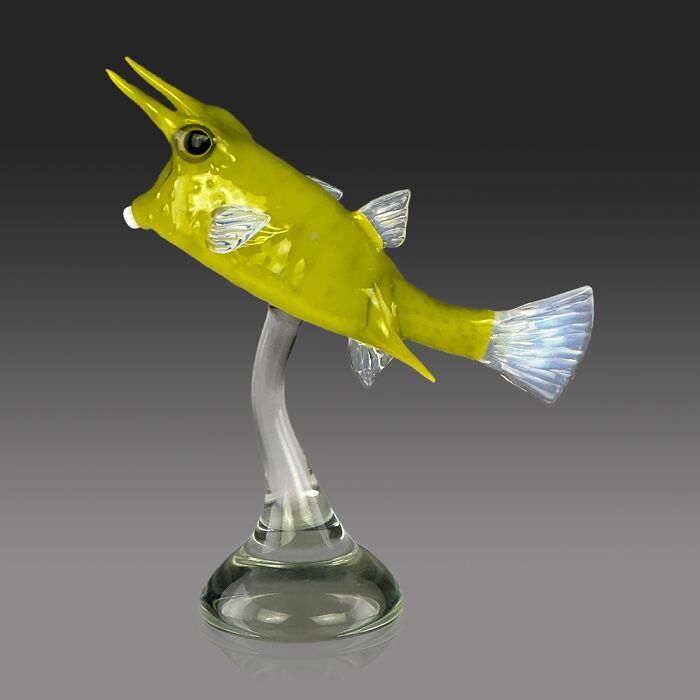 Yellow glass sculpture of an ocean fish with translucent fins on a clear glass stand showcasing stunning glass art.