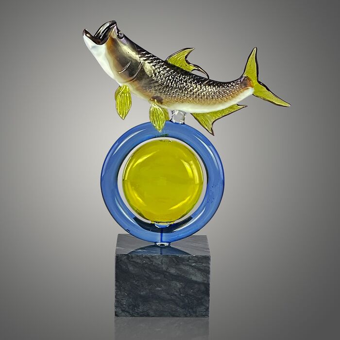 Glass sculpture of a fish with yellow fins mounted on a blue and yellow circular base, showcasing ocean life artistry.