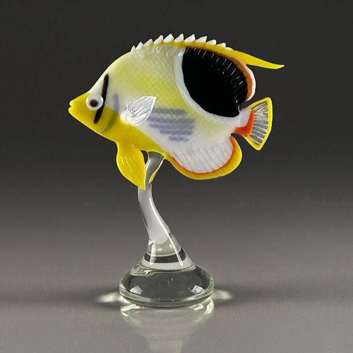 Yellow and black glass sculpture of a tropical fish on a clear glass stand, showcasing ocean life artistry.