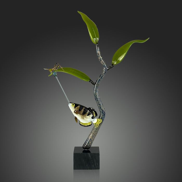 Glass sculpture of ocean life featuring a colorful fish and insect on green glass leaves with a twisted glass stem.