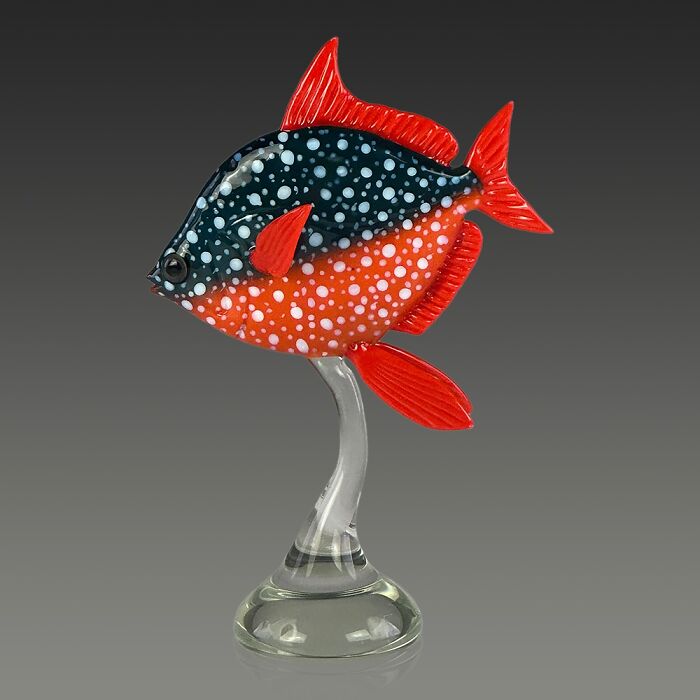 Glass sculpture of a vibrant ocean fish with red fins and a speckled black and orange body on a clear stand