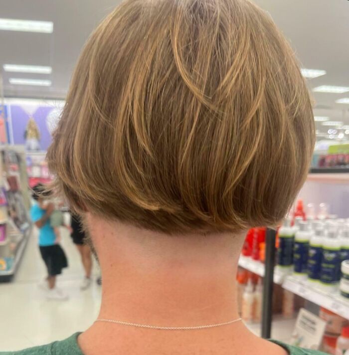 Woman with a short, uneven haircut showing a hilariously tragic hair accident in a store aisle background.