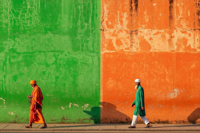 Two men walking past vibrant green and orange walls, capturing the beauty of everyday life in India by street photography.