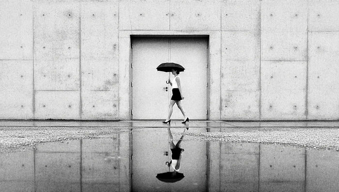 Woman walking with umbrella reflected in water, capturing the beauty of everyday life in India by street photographer.