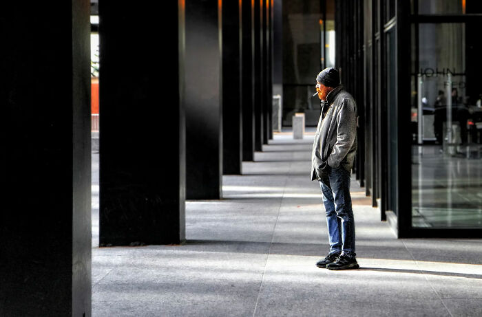 Man wearing a jacket and beanie standing thoughtfully under shadows in urban street, capturing the beauty of everyday life in India.