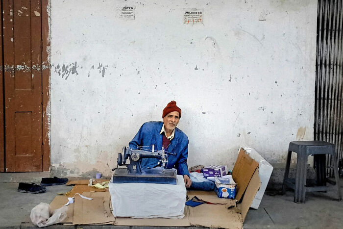 Street photographer captures everyday life in India showing a man sewing outdoors with a vintage sewing machine on a street.