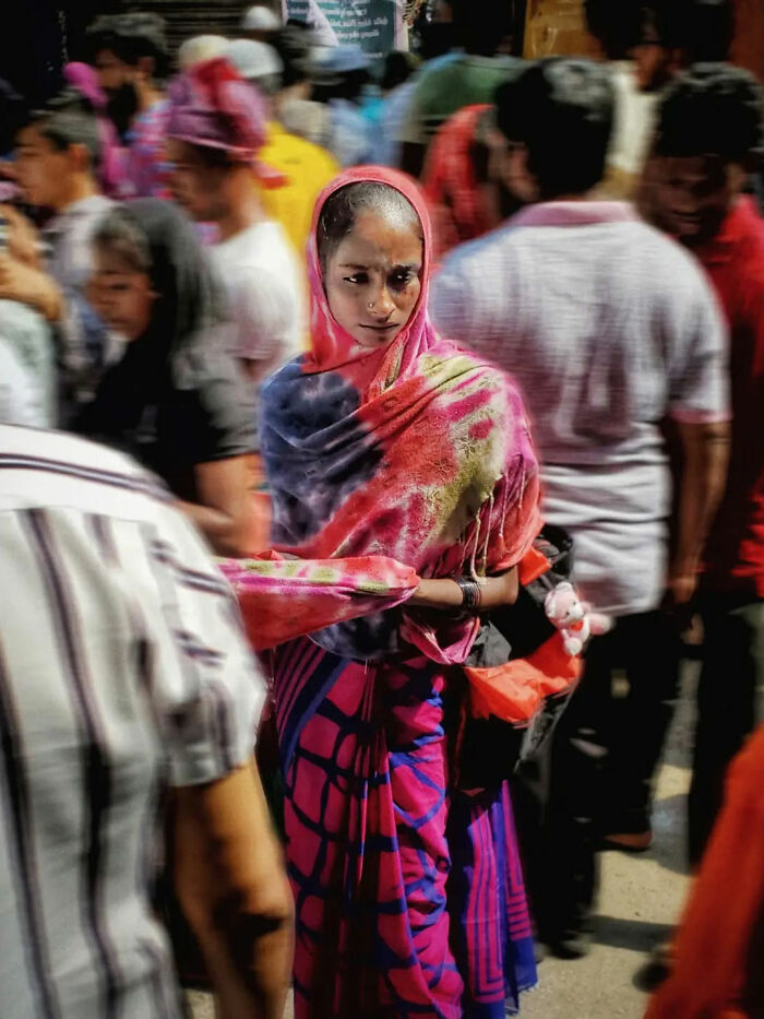 Young woman in colorful traditional attire standing in a busy street, capturing the beauty of everyday life in India by a street photographer