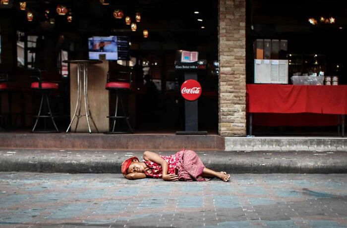 Child sleeping on pavement outside a café, capturing the beauty of everyday life in India by street photographer.