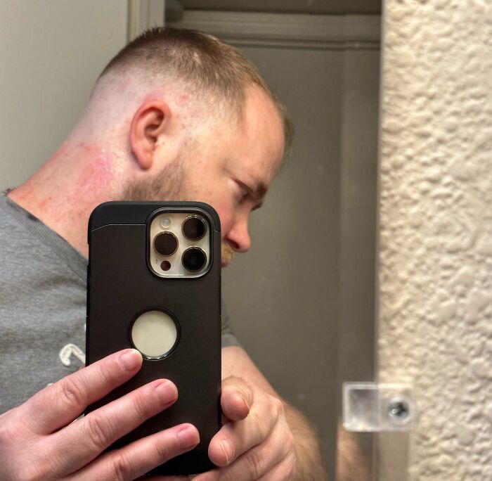 Man taking a mirror selfie showing a tragically uneven and patchy haircut in a casual indoor setting.