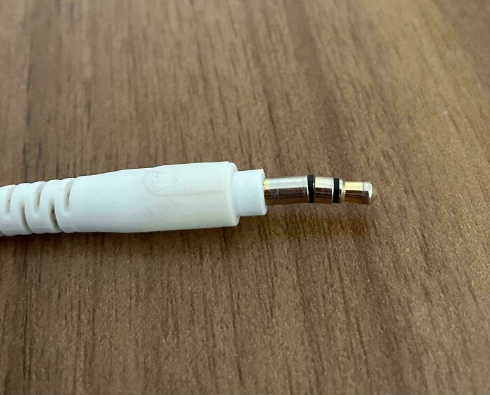 White headphone jack plug resting on a wooden surface, illustrating everyday frustrations shared by family members online.