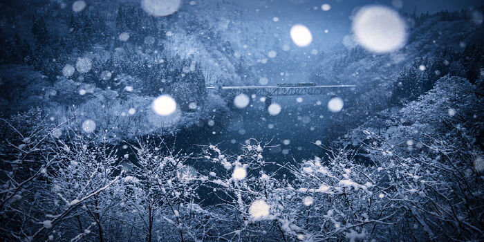 Snowfall over a frozen lake with snow-covered trees during winter, a panoramic masterpiece capturing serene nature's beauty.