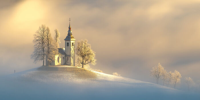 Panoramic masterpiece of a hilltop church surrounded by frosted trees under a soft glowing sky, awarded in Epson Pano Awards.