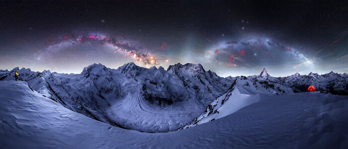 Panoramic night mountain landscape under a starry sky with the Milky Way visible, featuring snow and tents.