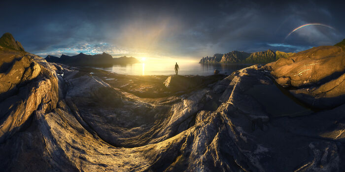Dramatic panoramic landscape showing rocky foreground, lone figure, and glowing sunset over distant mountains, Epson Pano Awards.