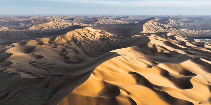 Panoramic desert landscape with expansive sand dunes under a clear sky, showcasing stunning natural patterns and shadows.