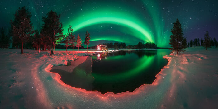 Aurora borealis glowing over a snowy landscape with a lake reflecting the panoramic masterpiece scene.