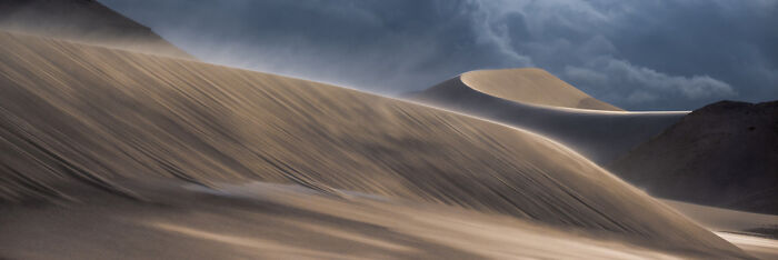 Sweeping panoramic view of sand dunes under dramatic cloudy sky, showcasing stunning landscape photography techniques.