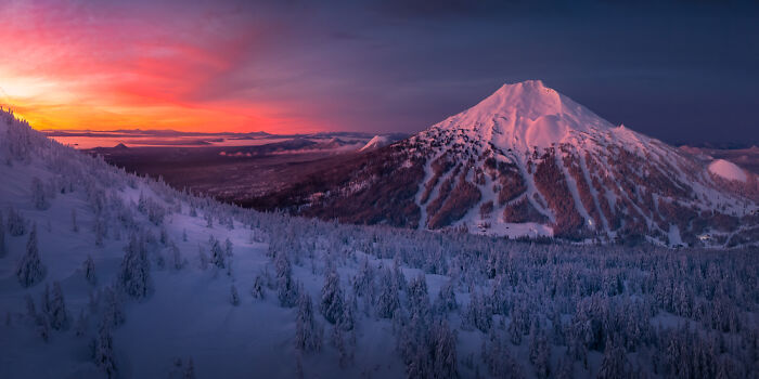Panoramic masterpiece of a snow-covered mountain at sunset showcasing vibrant sky hues and winter forest landscape.