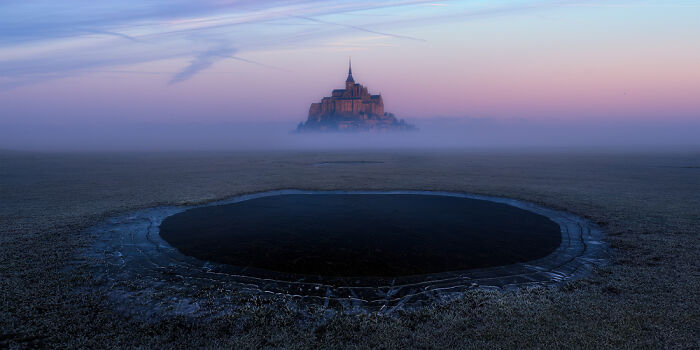Foggy landscape with a mysterious circular pond and a distant illuminated structure, showcasing panoramic masterpieces.