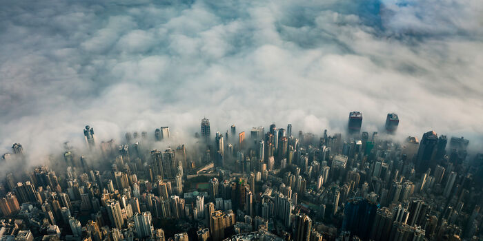 A panoramic aerial view of a cityscape with skyscrapers emerging through a dense layer of fog.