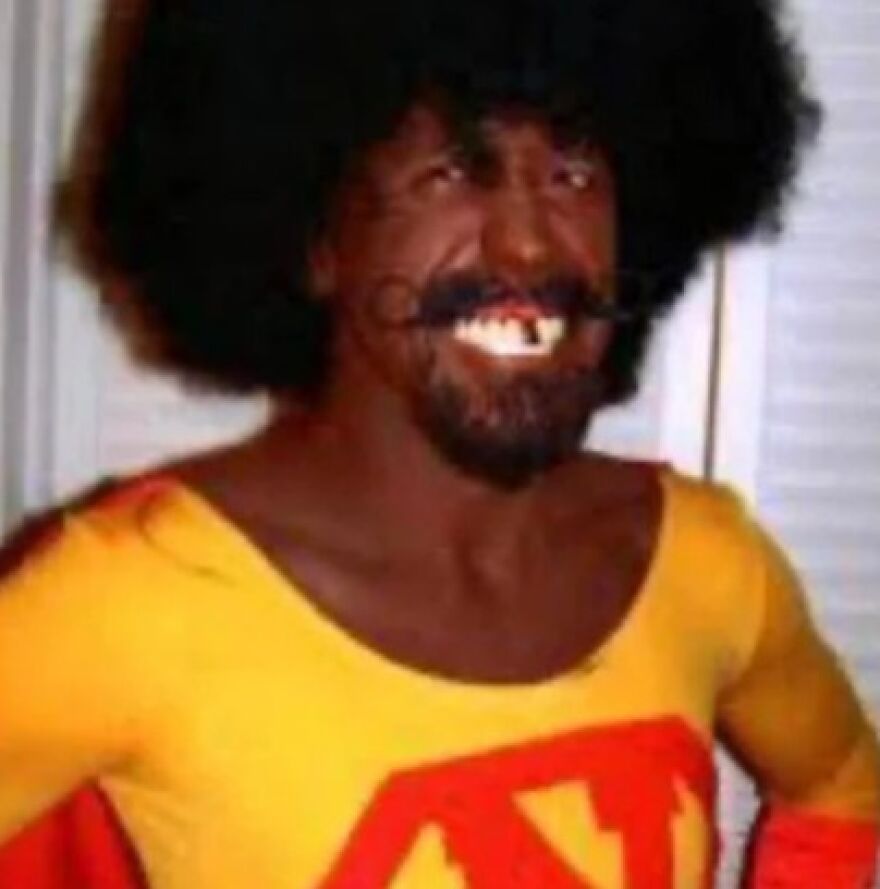 Man in a yellow and red superhero costume with exaggerated teeth and a large afro showcasing lack of common sense Halloween costume.