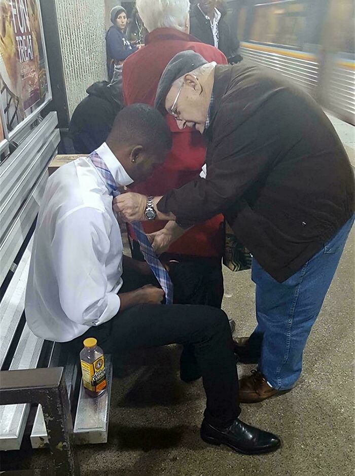 Older man helping a stranger tie his necktie at a bus stop, showcasing faith in humanity restored through kindness.