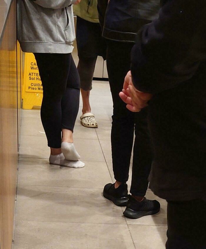 Several people standing in a line indoors, showing diverse footwear and casual clothing in a public setting.