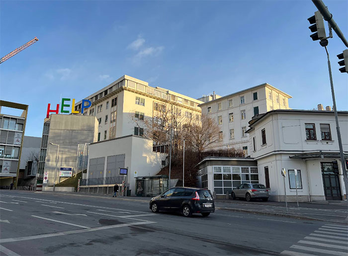 Hospital building with colorful HELP sign on rooftop, cars on street, and clear blue sky in the background. Hospital building with colorful HELP sign on rooftop, cars on street, and clear blue sky in the background.