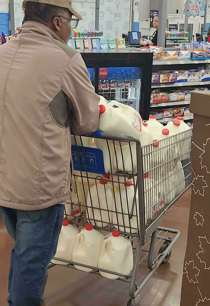 Man at Walmart pushing a cart full of gallon milk jugs in a store aisle near the checkout counter