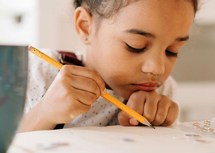 Young girl focused on drawing with a pencil, illustrating concentration and mental health awareness concepts.
