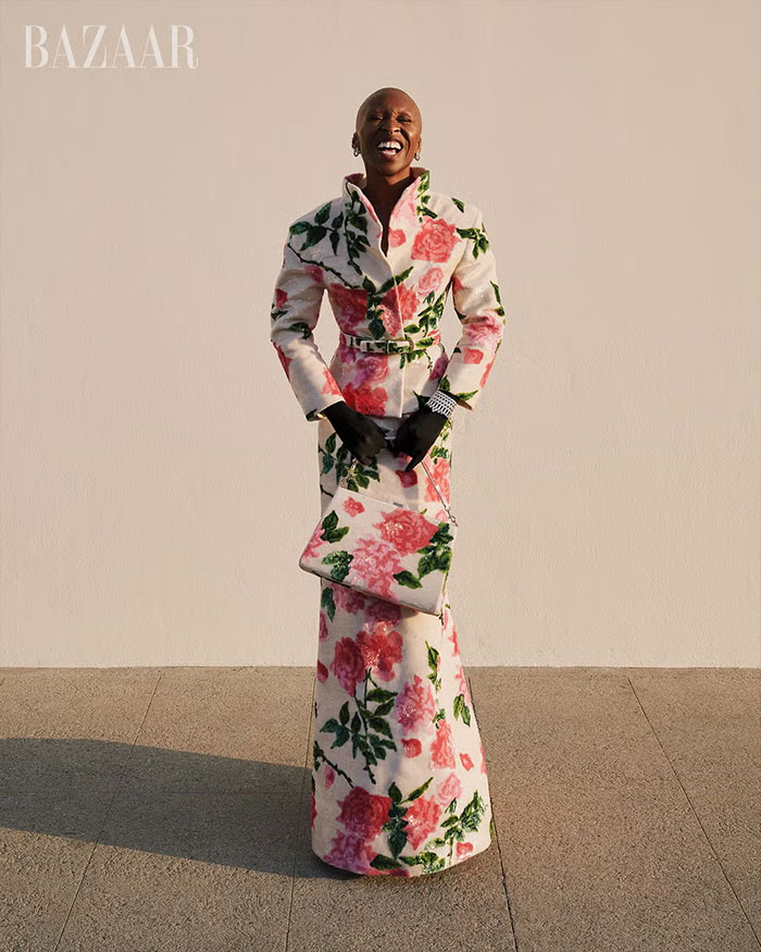 Cynthia Erivo in floral patterned coat dress and matching bag posing for controversial Harper’s Bazaar shoot outdoors. Cynthia Erivo in floral patterned coat dress and matching bag posing for controversial Harper’s Bazaar shoot outdoors.