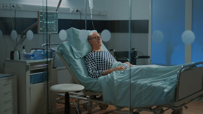 Elderly patient lying in a dimly lit hospital bed with medical equipment nearby, evoking scary ghost stories at work.