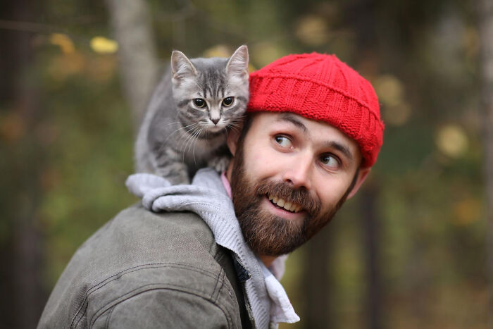 Man smiling outdoors with a gray cat on his shoulder, illustrating the most destructive thing cat ever done concept.