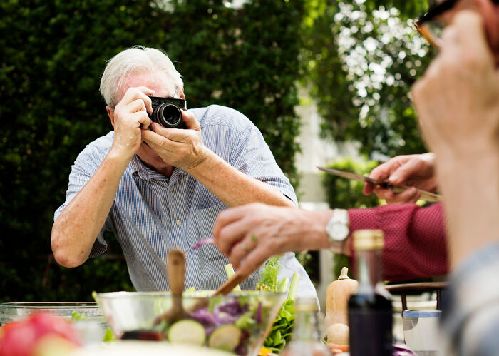 Older man struggling with camera settings while taking photos at a family gathering.