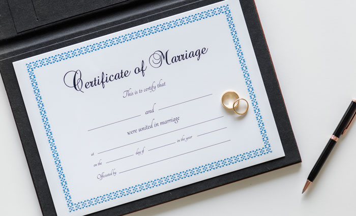 Marriage certificate with two gold wedding rings and a black pen, symbolizing wedding sabotage before the ceremony.